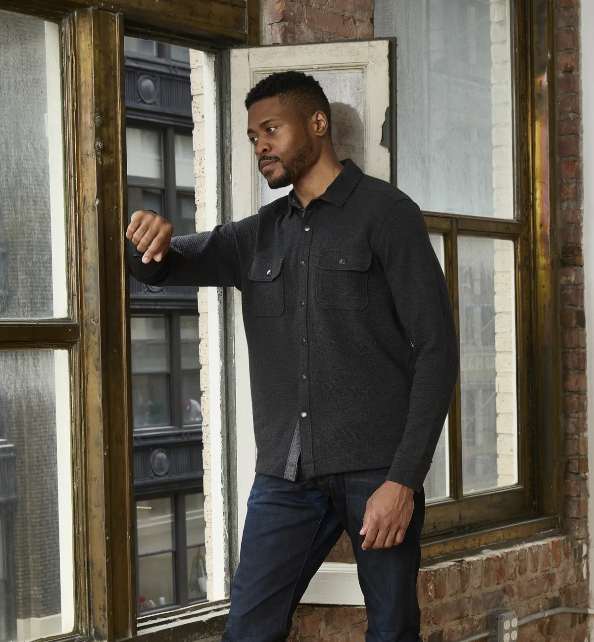 Original Nicoby model walking by a window in the black Snap-Front Knit Overshirt