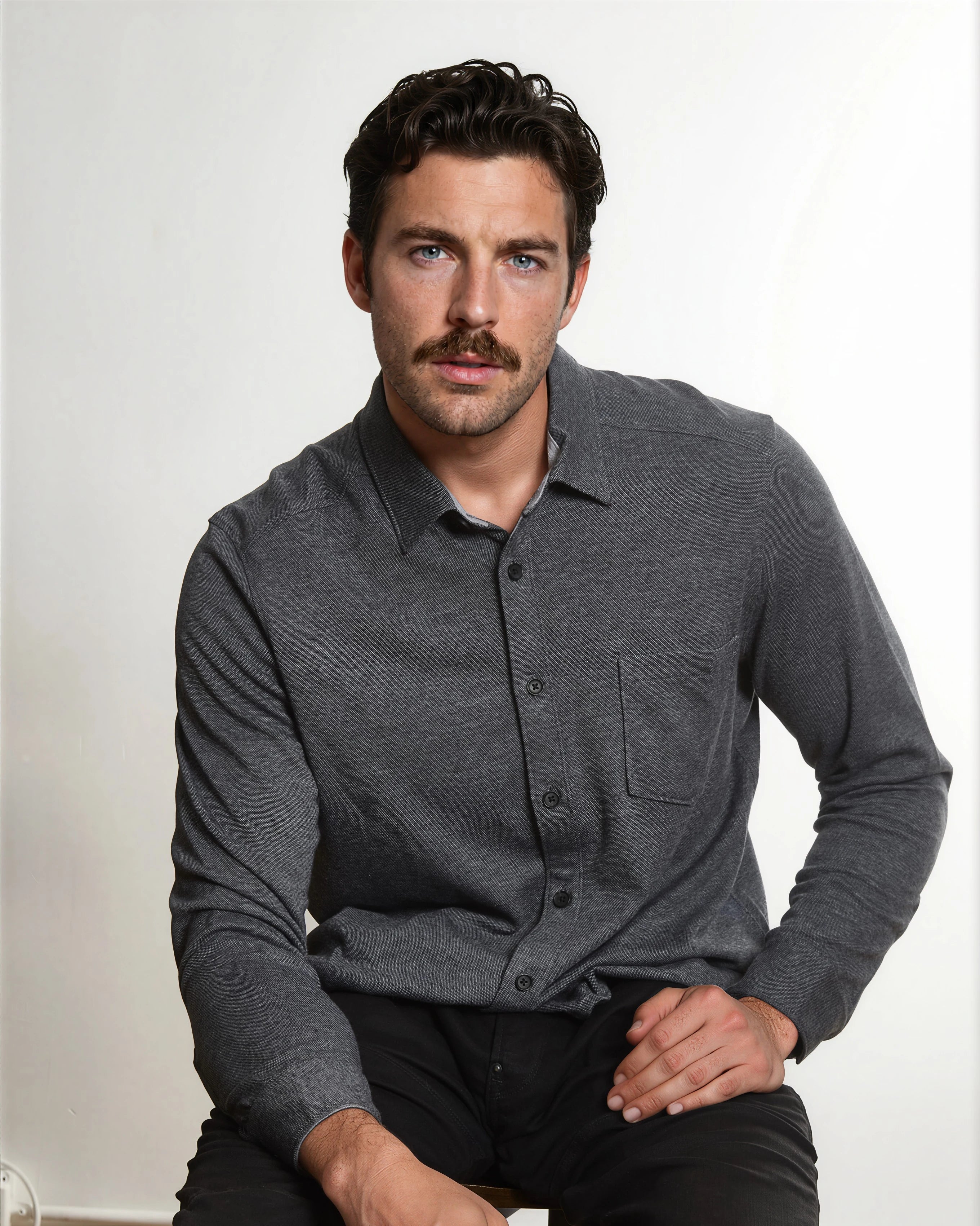 Seated mustached model wearing the black Heather Birdseye Double-Face Knit Shirt